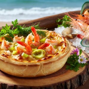Torta reta gourmet de camarão e alho-poró, crocante e cremosa, sobre prato branco. Fundo litorâneo brasileiro com mar azul, ervas frescas e frutos do mar.