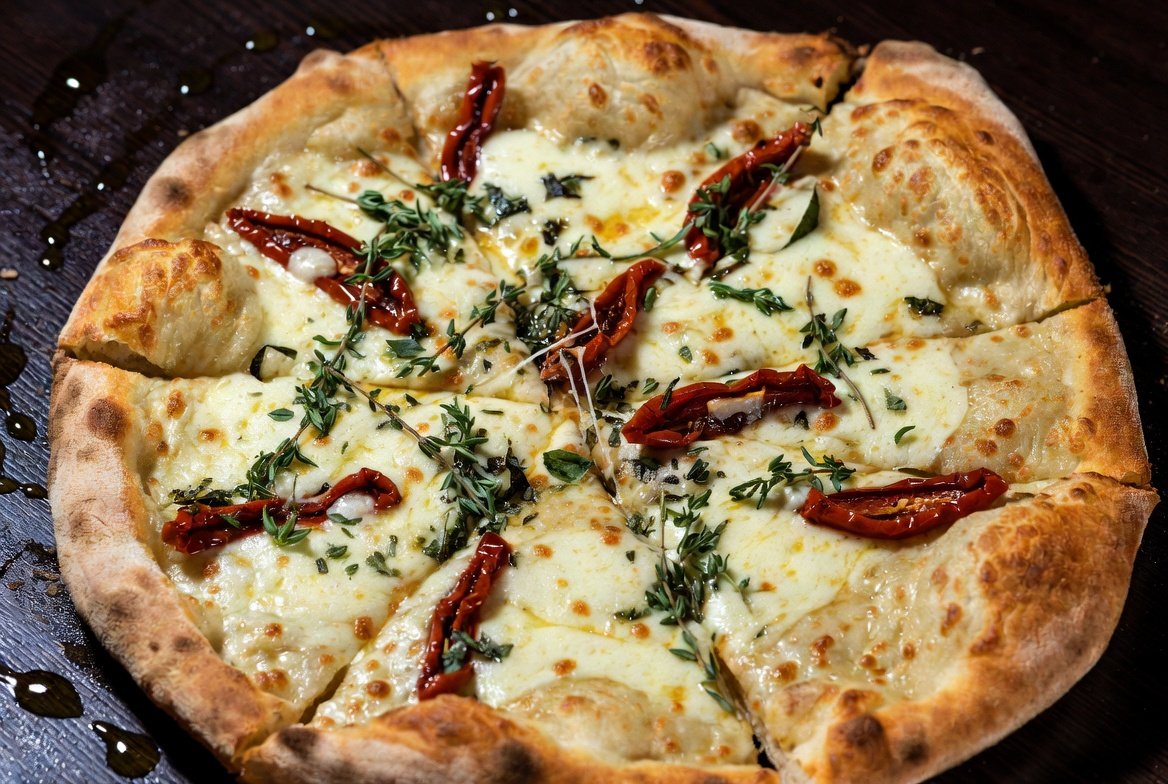 Pizza de Mandioca Mutante gourmet: base crocante dourada de mandioca, queijo mussarela derretido, tomate seco e ervas frescas aromáticas.