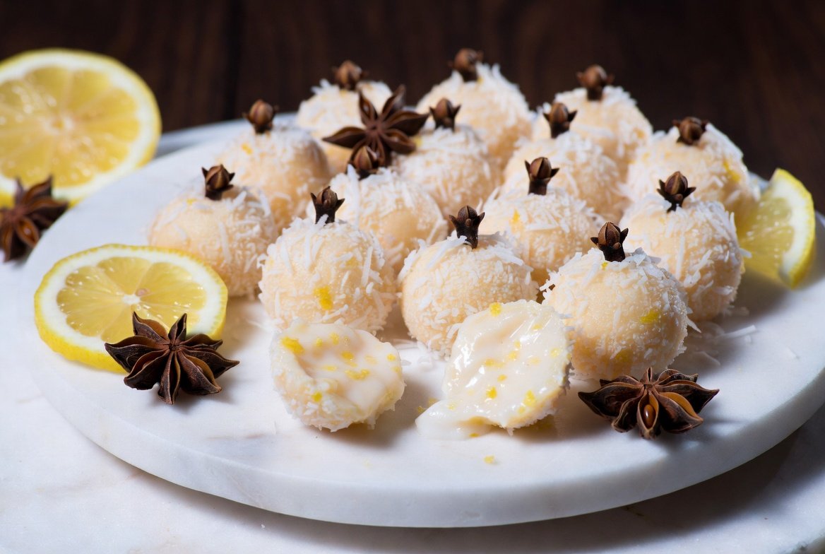 Beijinho Traidor: docinhos cremosos de coco polvilhados com coco ralado, toque azedo de limão, cravo e raspas cítricas em prato de mármore gourmet.