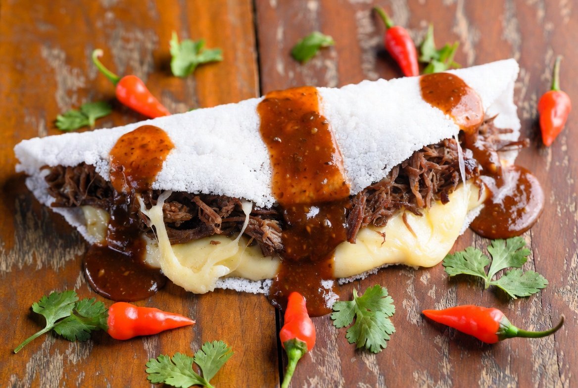 Tapioca do dragão Tapioca do Dragão – Fogo na Boca: crocante por fora, recheada com carne seca, queijo coalho derretido e molho picante de pimenta dragão. Criação gourmet Root Taste.